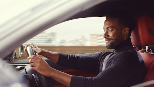Man smiling in blue jumper driving a car with red seats